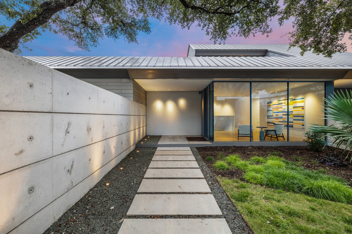 Dusk view of the entry walk at 3407 Monte Vista Dr, a board-formed concrete wall leading to a glass-walled modern home