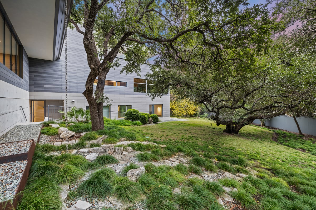 Native grasses and limestone boulders under live oaks beside the clad front wing