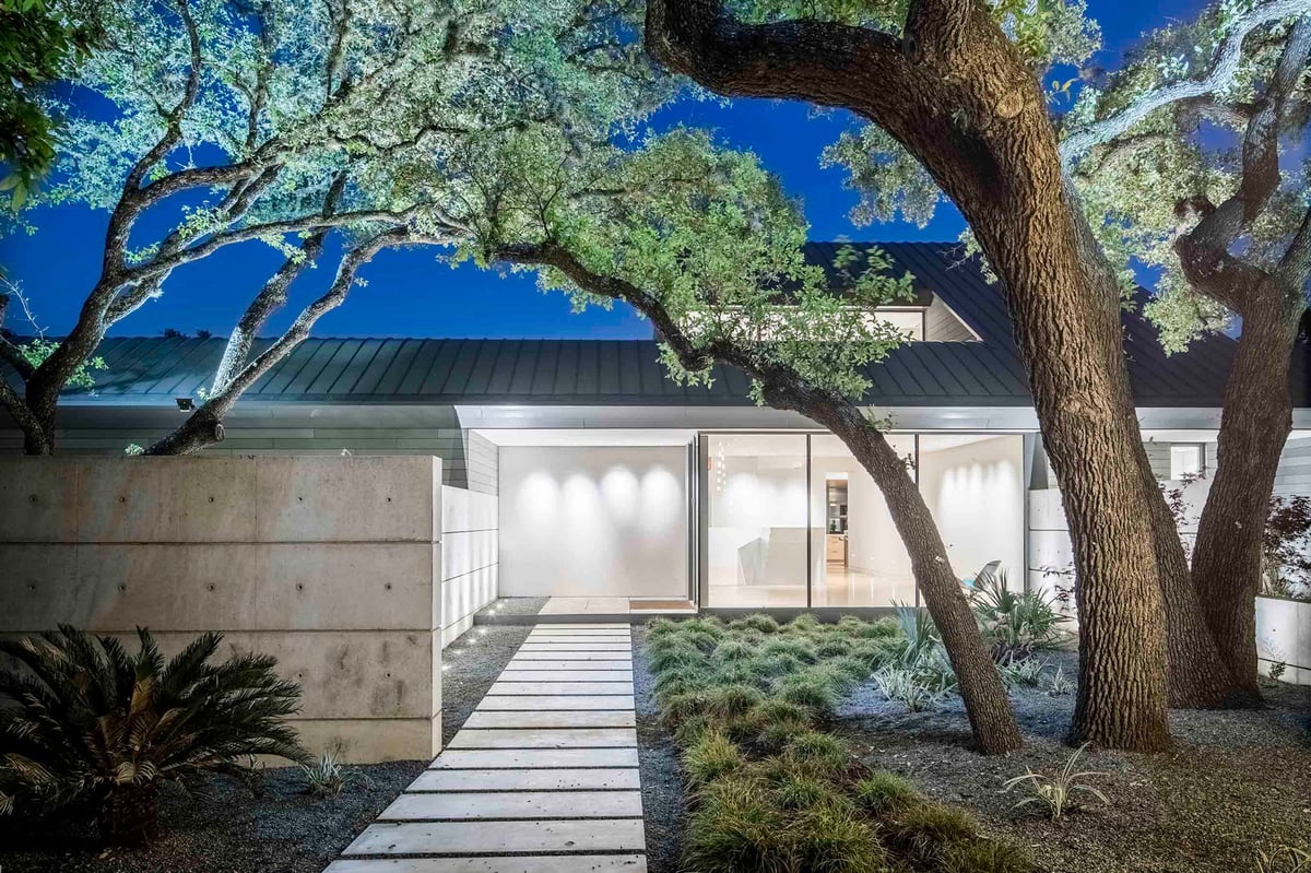 The front walk under spreading live oaks at dusk, the entry glowing ahead