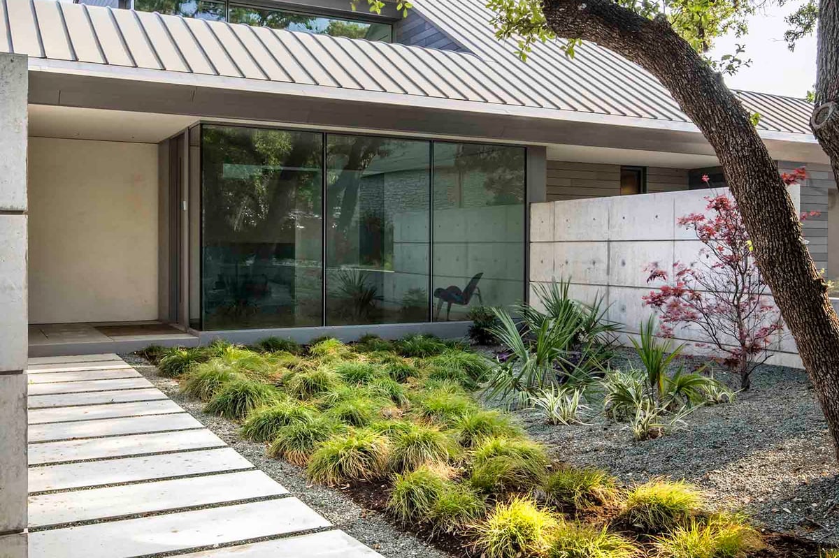 Paver walk through grasses to the glass entry beside a concrete wall