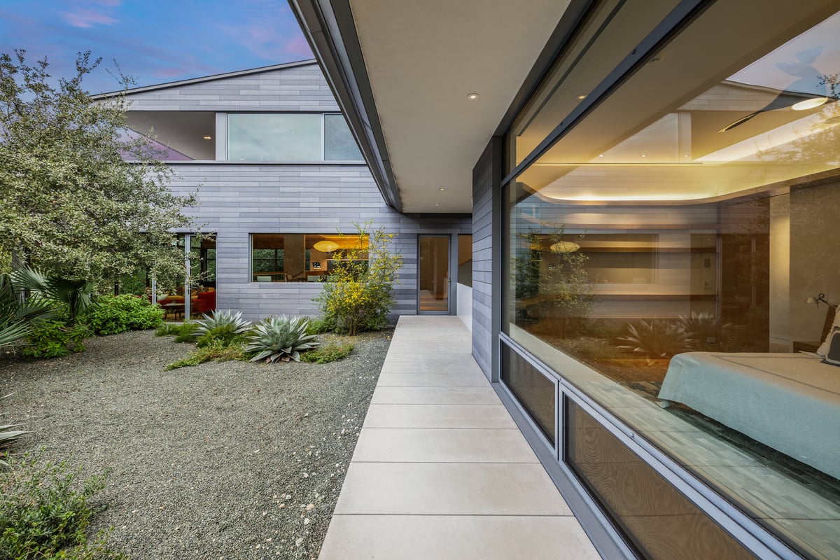 Covered side walk along a glass wall of the house with a gravel garden and oaks outside