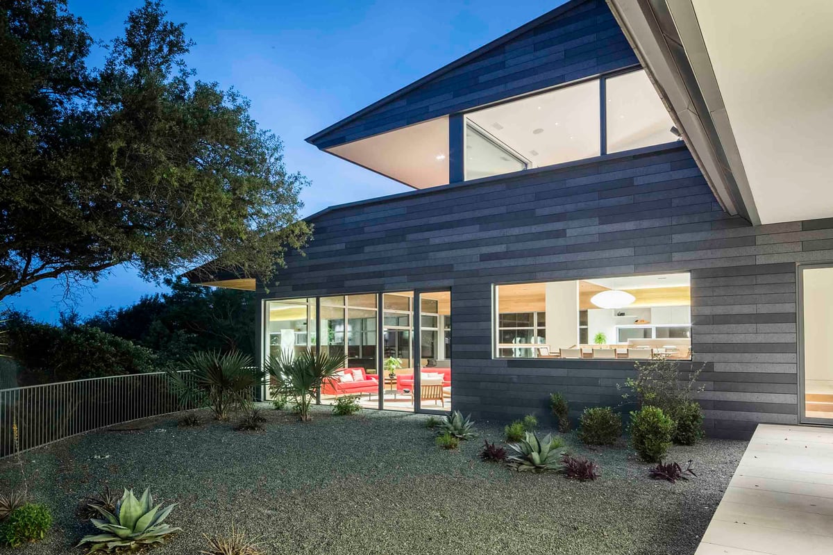 The cantilevered upper wing at dusk above a lit living level and gravel garden