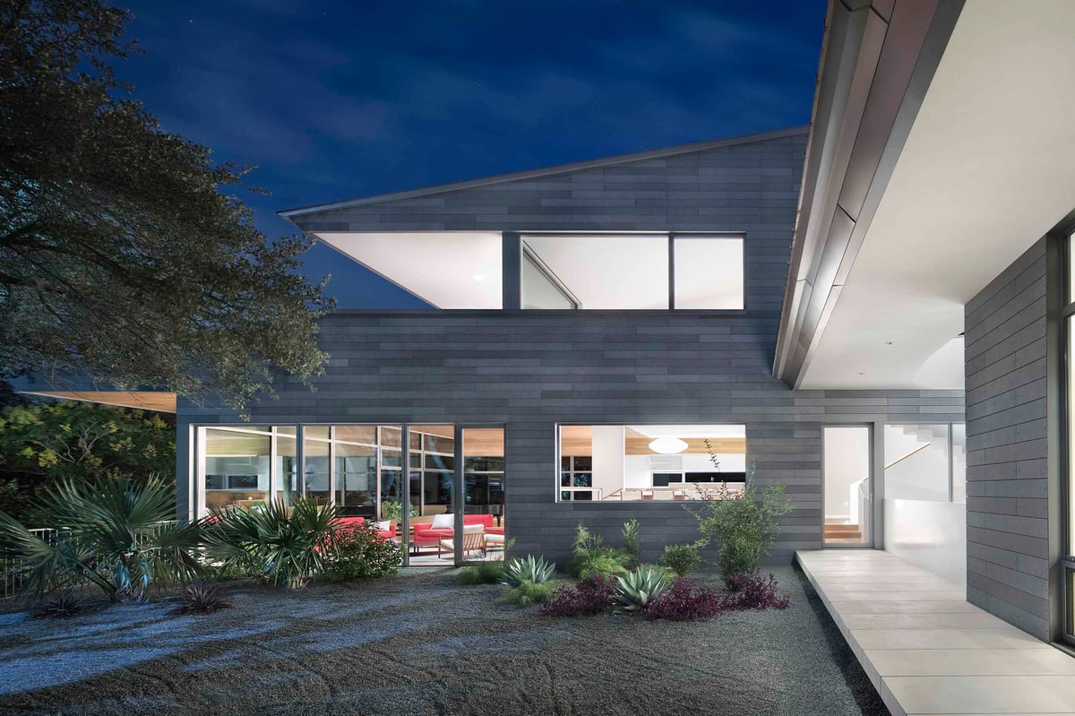 The living wing at dusk, lit rooms behind glass above a planted bed