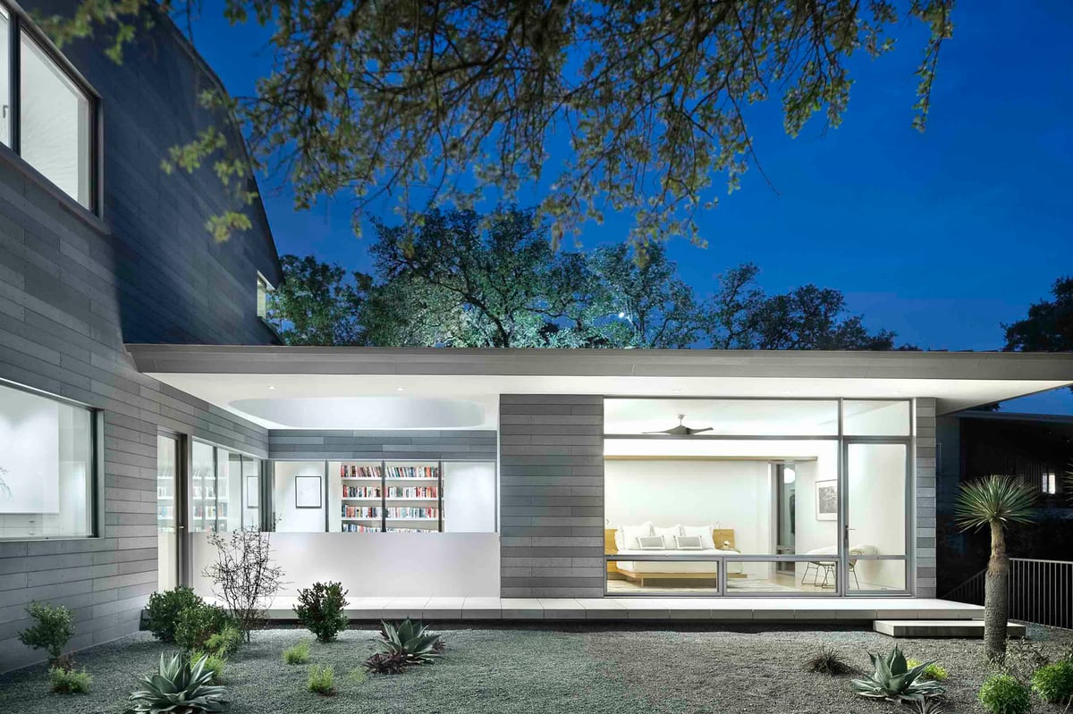 The rear wing at twilight, a lit room behind glass and a gravel garden