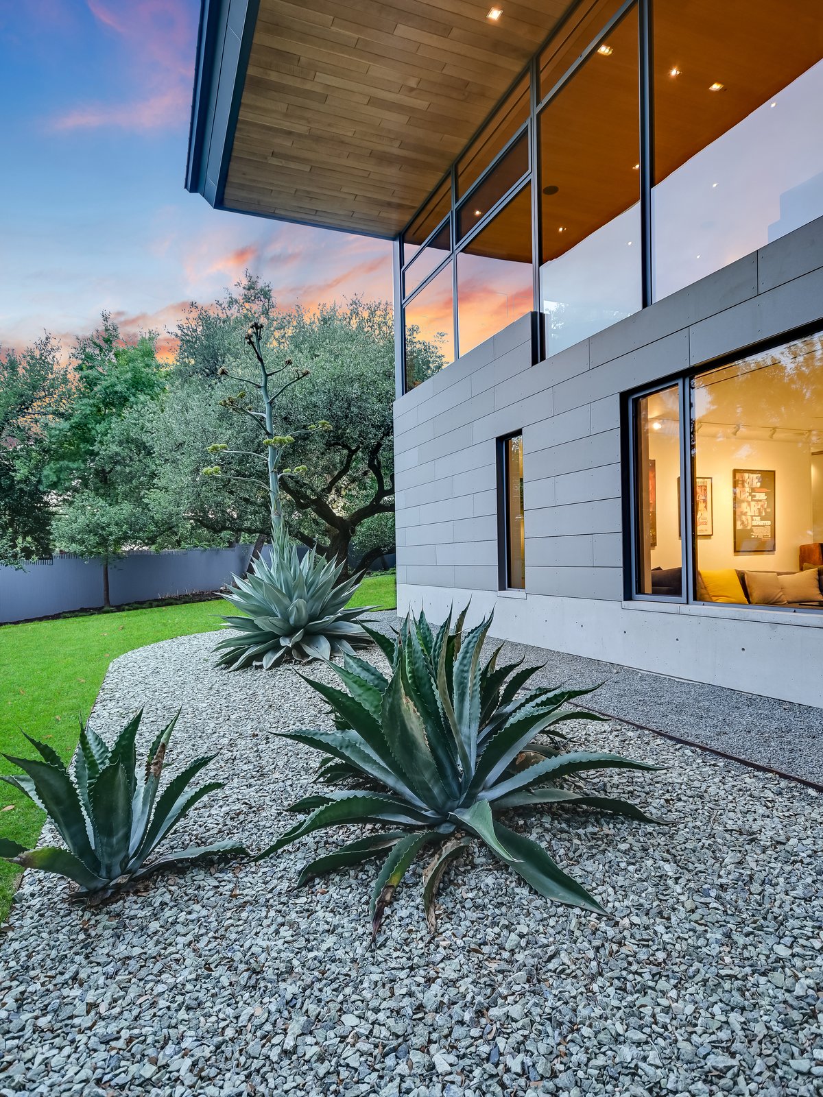 Clad wall and lit windows above an agave and gravel bed
