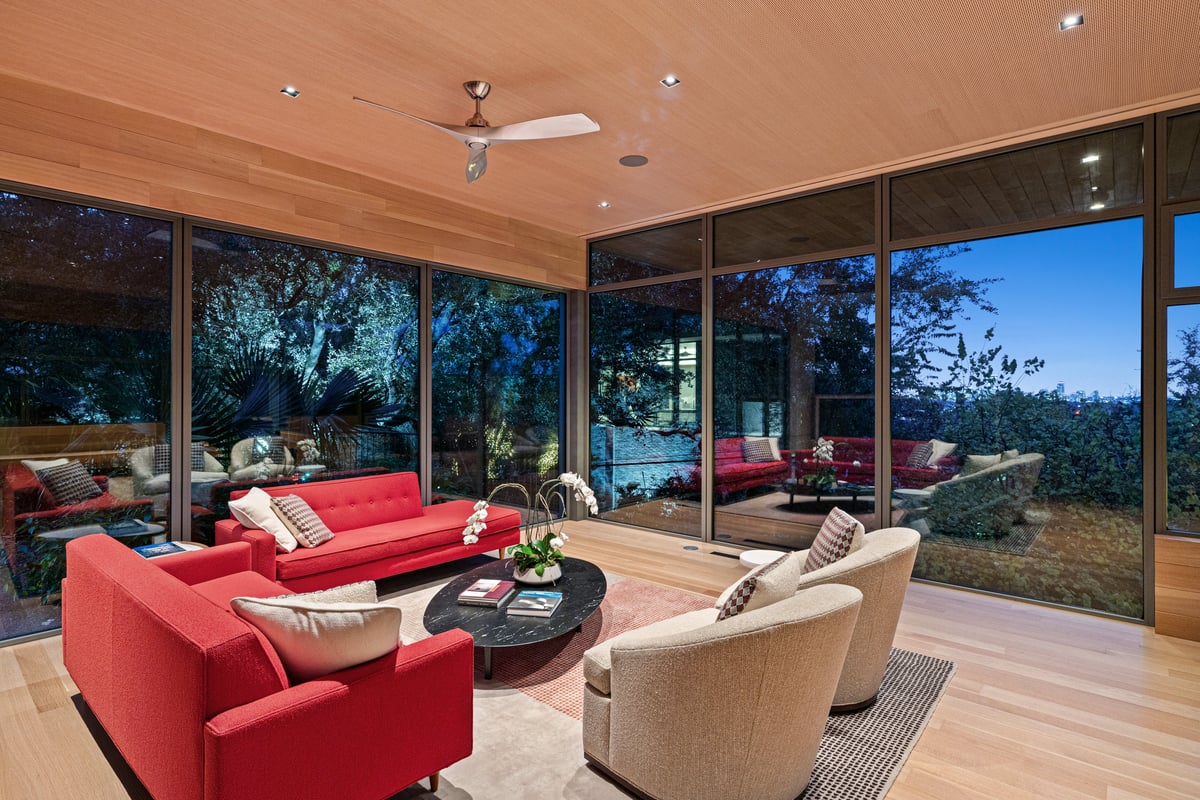 Great room at dusk with floor-to-ceiling glass, a wood ceiling and the tree canopy beyond