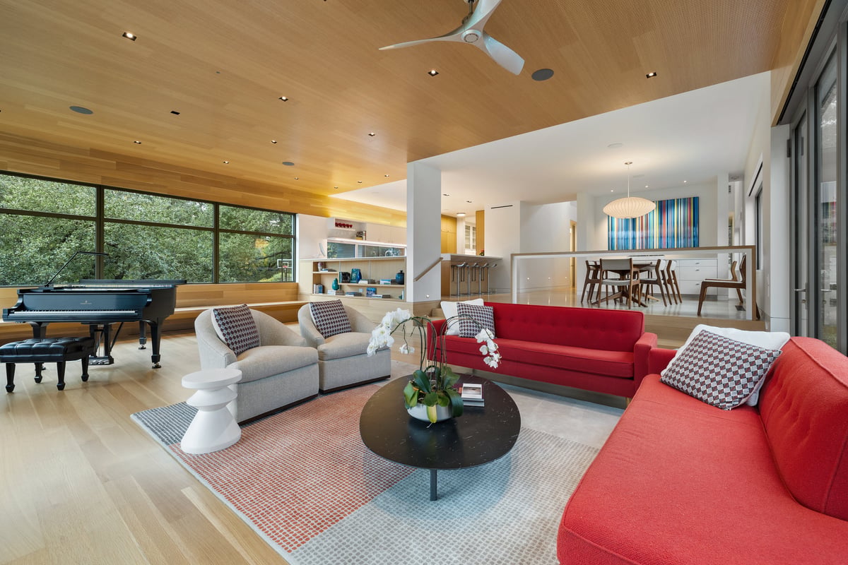 Great room seating around a round coffee table with the kitchen and piano beyond