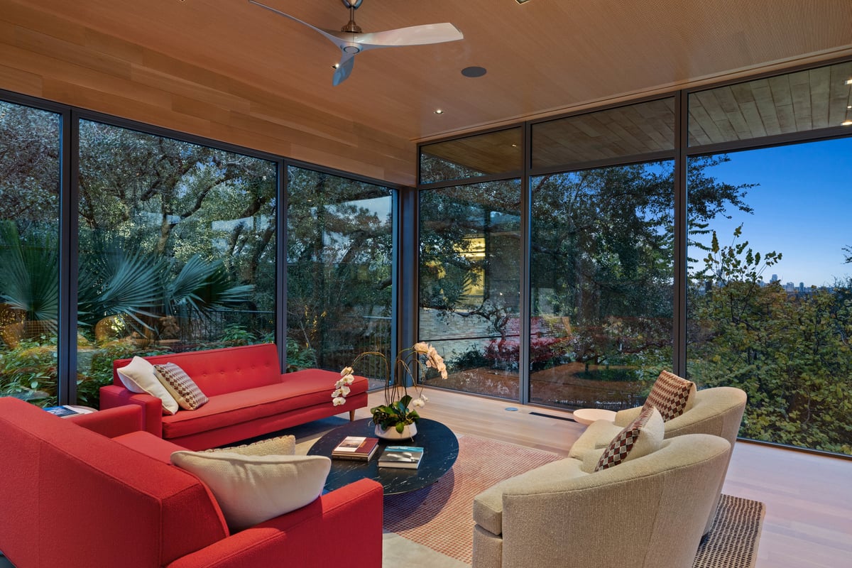 Great room corner at dusk, red sofas against two walls of glass and a lit garden