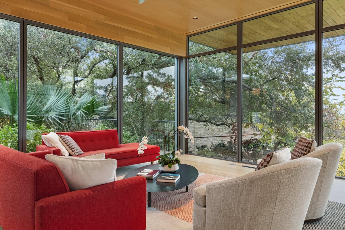 Great room seating around a round coffee table, palms and oaks through the glass