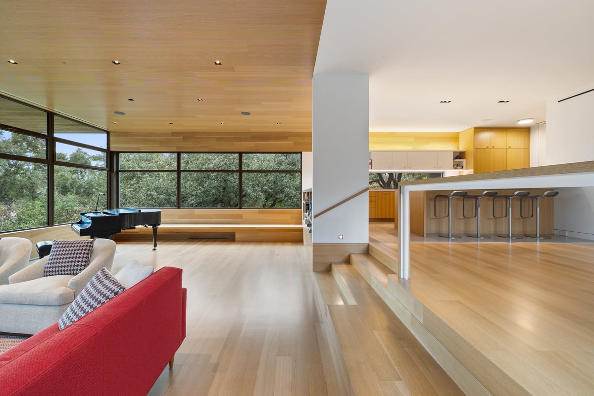 Great room steps rising to the kitchen level, with the piano by the windows