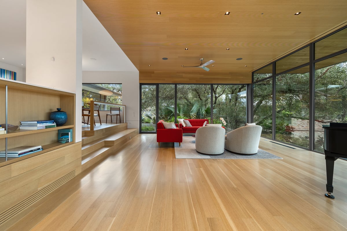 Great room with built-in shelving, the seating area and the piano against the glass