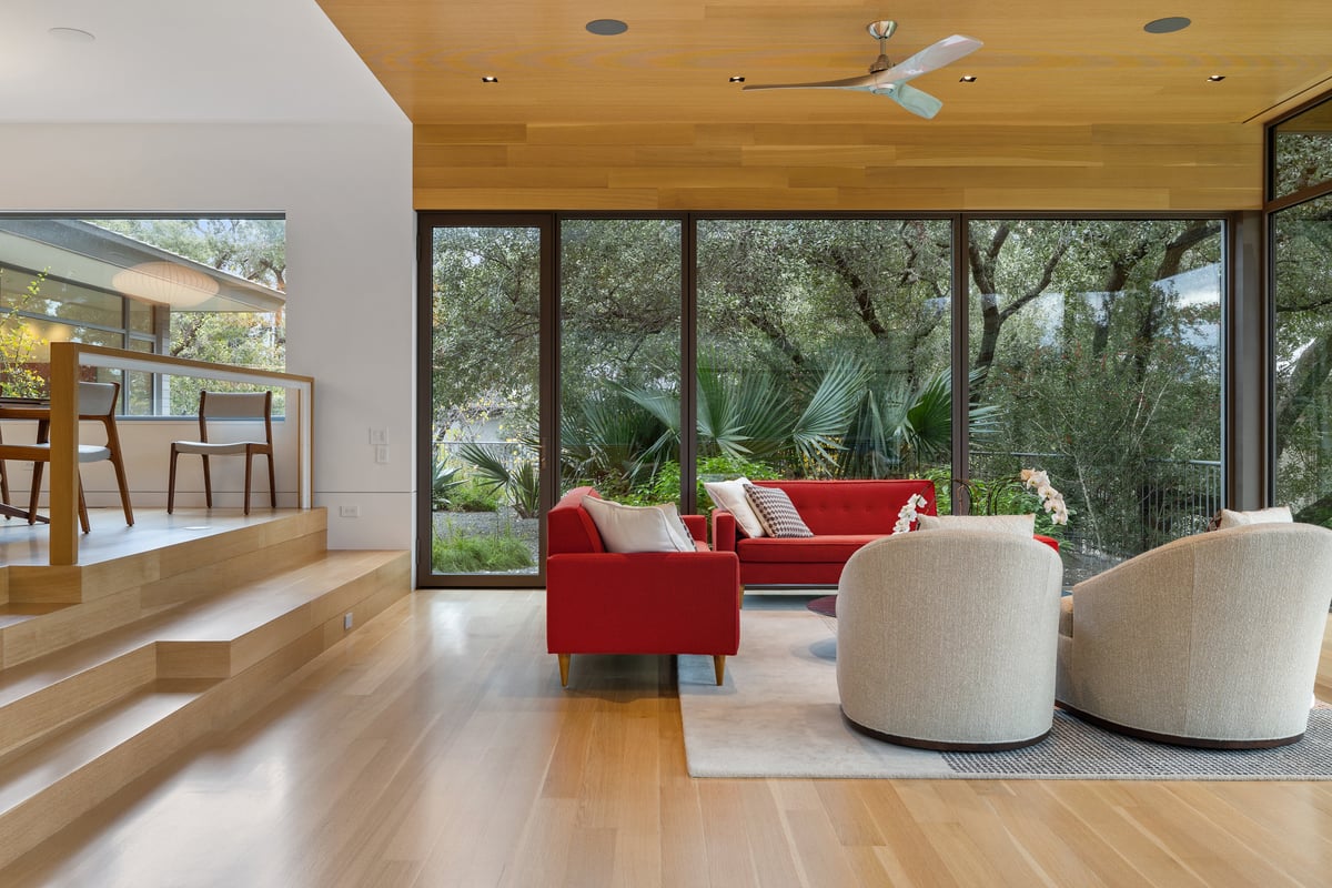 Great room seating seen wide, red sofa and swivel chairs under the wood ceiling