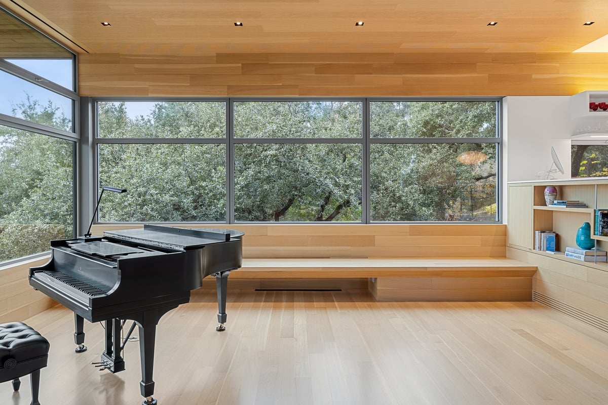 Grand piano beside a long built-in window bench and the tree canopy