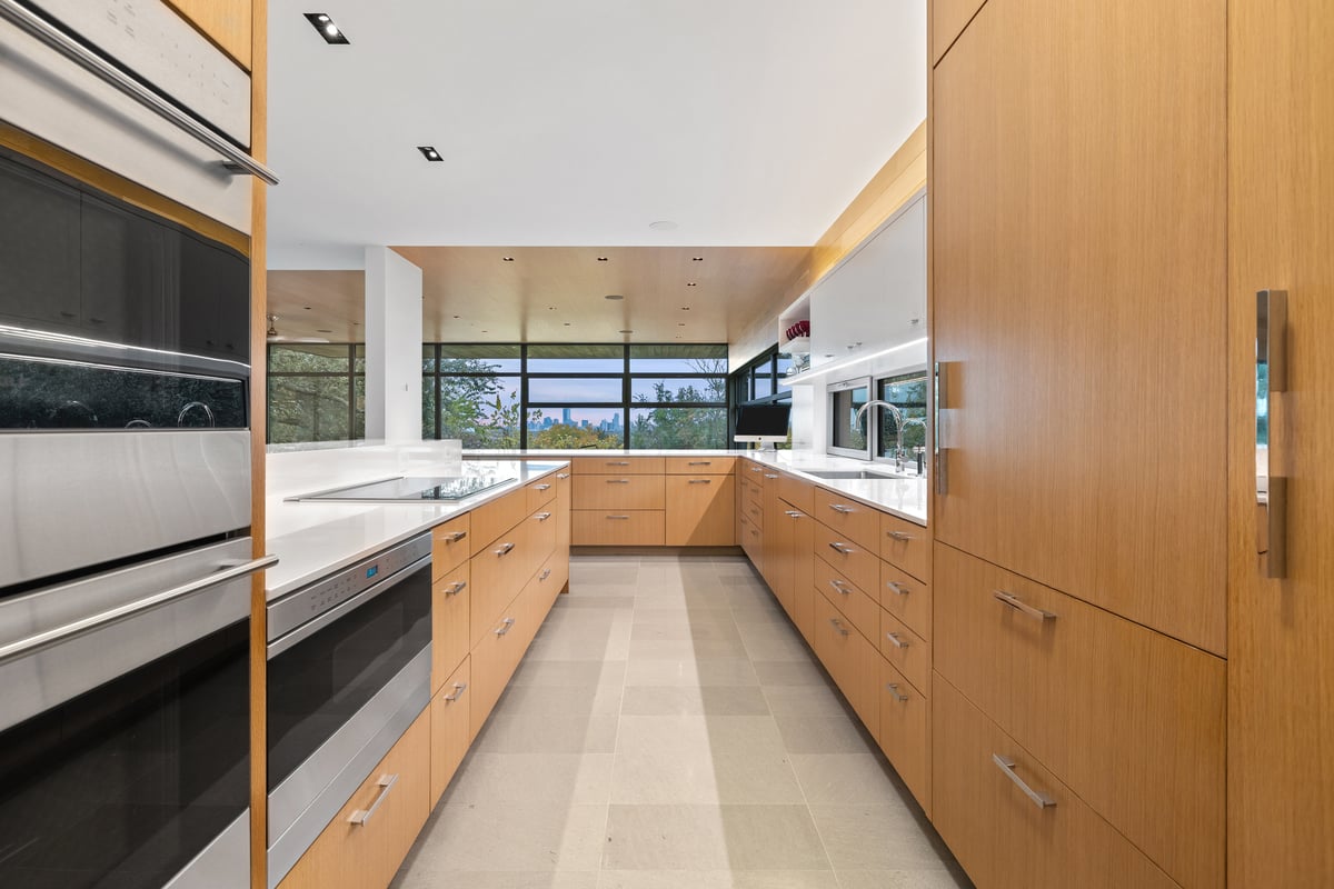 Galley kitchen with warm wood cabinetry, stone counters and a long window over the trees