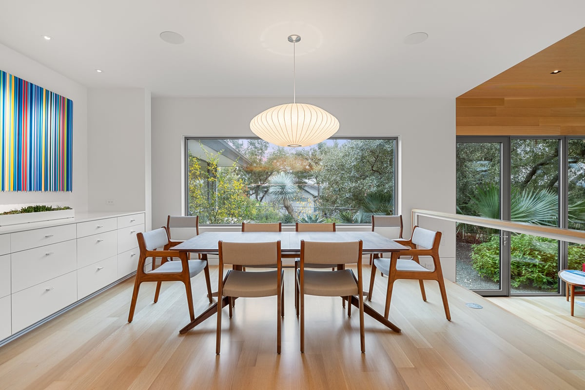 Dining room under a paper pendant with a wall of built-ins and a window to the trees