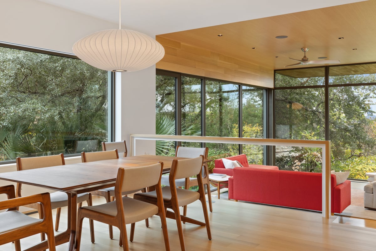 Dining table beside the great room with the glass wall and oaks beyond