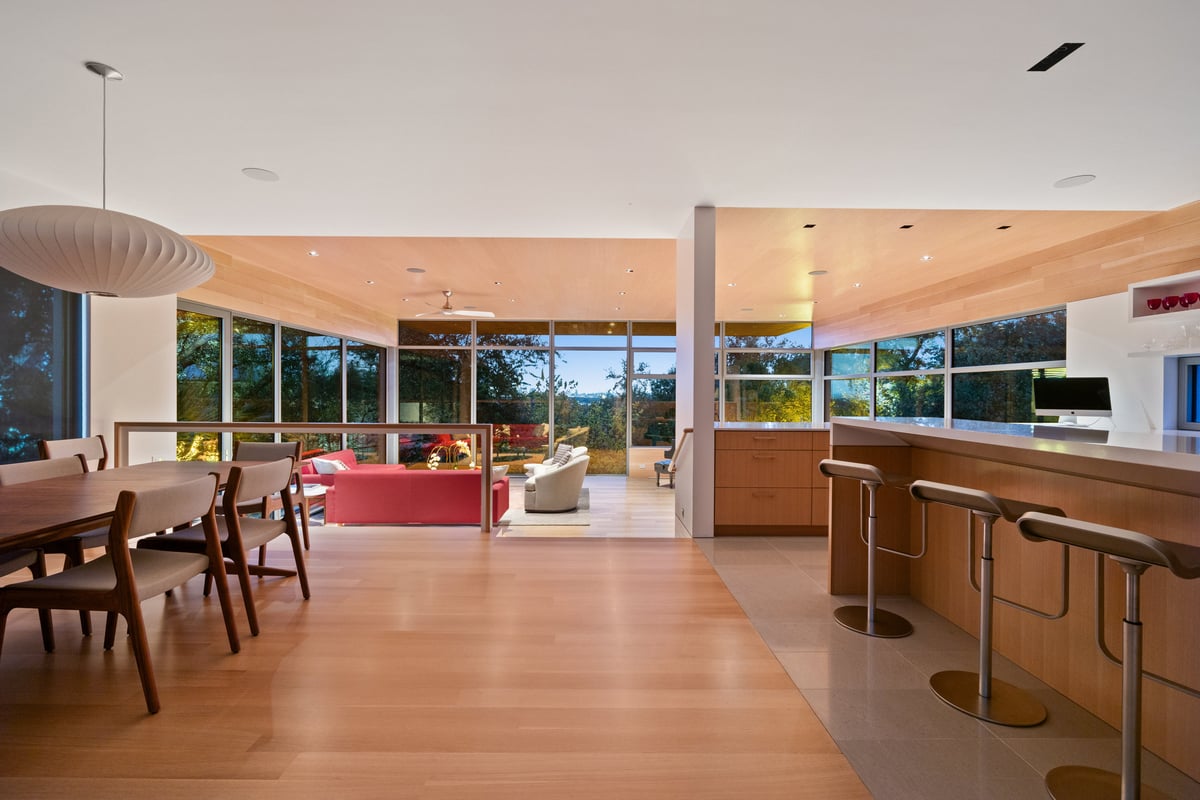 Dining table beside the kitchen bar, with the great room and its red sofas beyond the glass