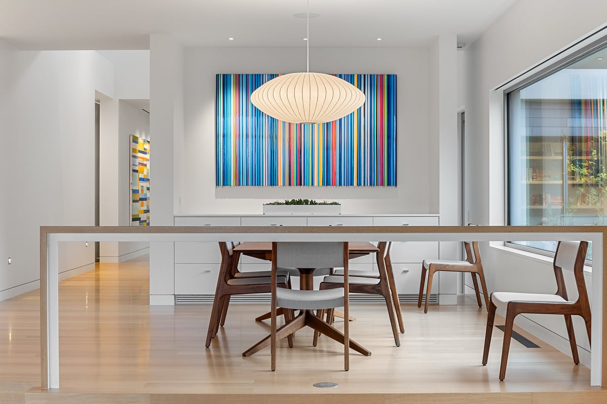 Dining table under a paper pendant, a striped artwork on the wall behind