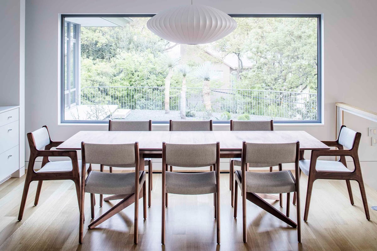 Dining table under a paper pendant facing a large window to the trees