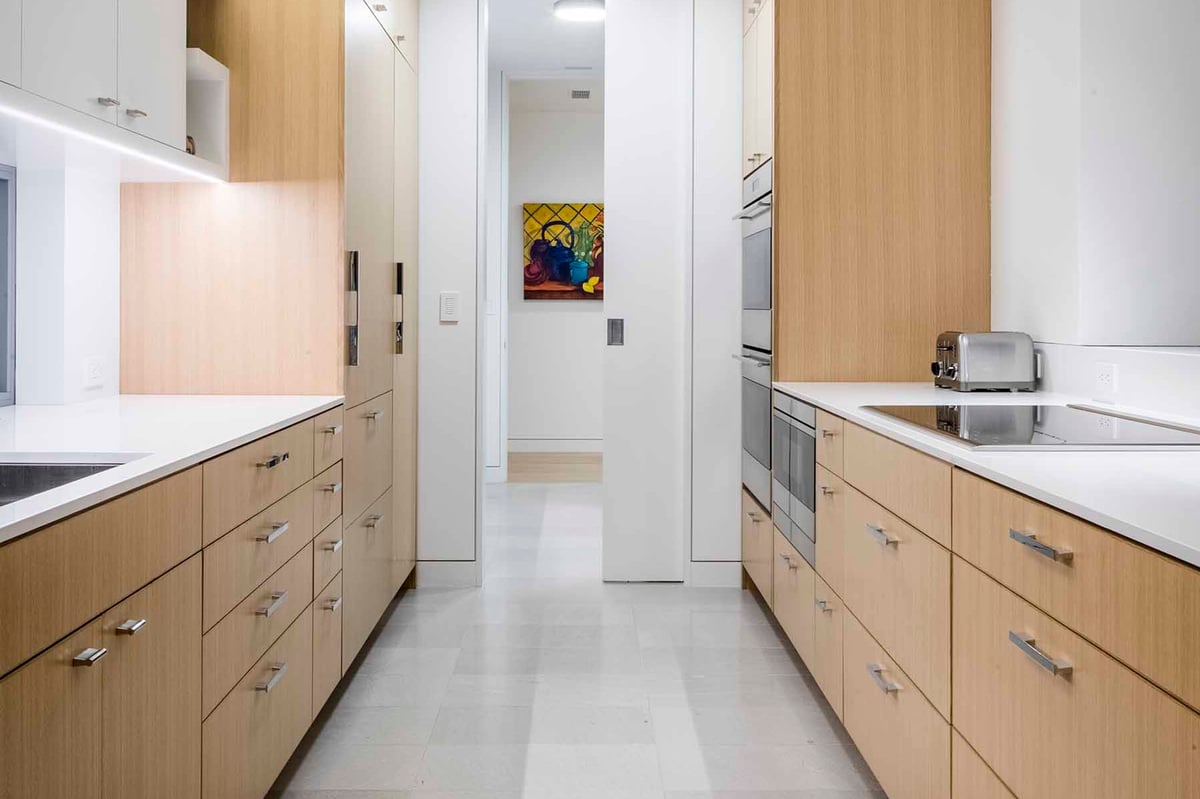 Galley kitchen with oak cabinetry and a colorful artwork at the end of the hall