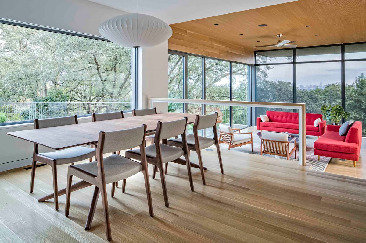 Dining table beside the great room, red sofas and the glass wall beyond