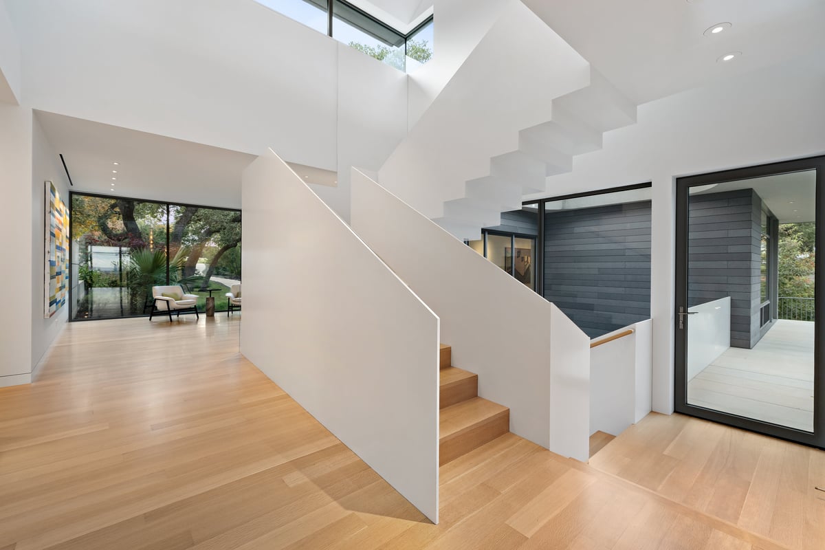 Sculptural white staircase beside a glass wall, light pouring in from above