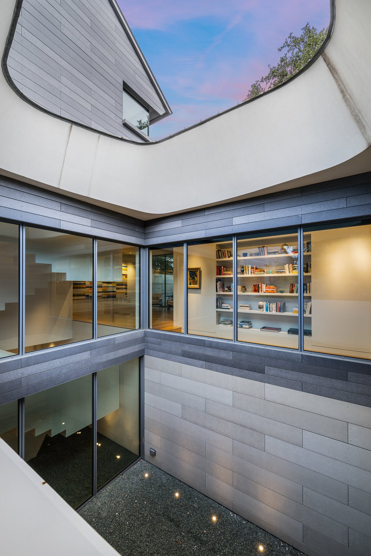 A skylit interior courtyard seen from above, glass walls and a bookshelf around a void