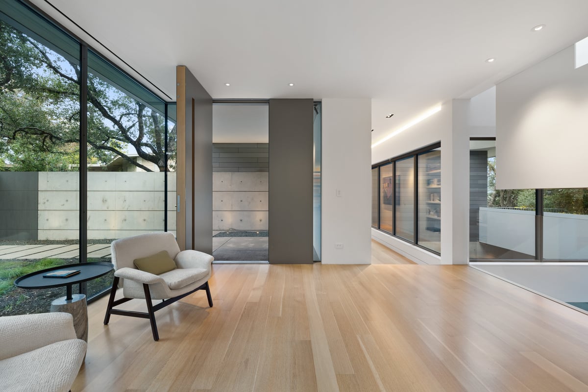 Gallery hall with a lounge chair, full-height glass and a walled garden outside