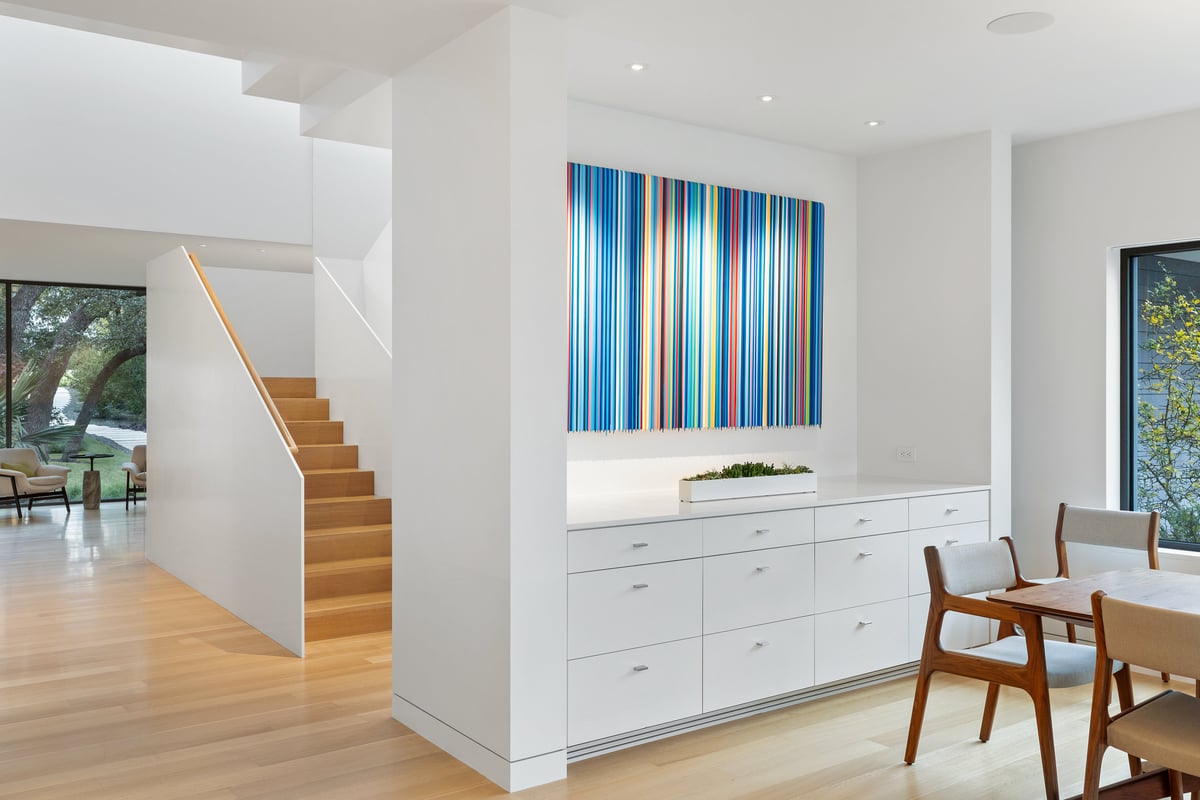 Oak stair rising beside white built-in cabinets and a striped artwork