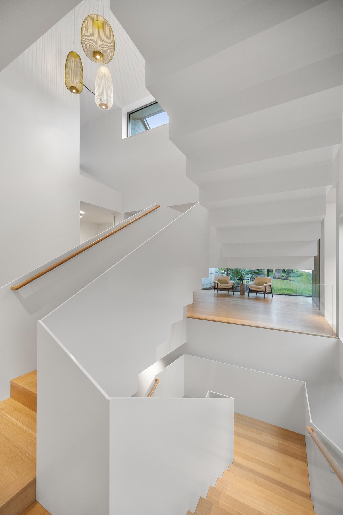 The white stair seen from the landing, a pendant light hanging in the stairwell