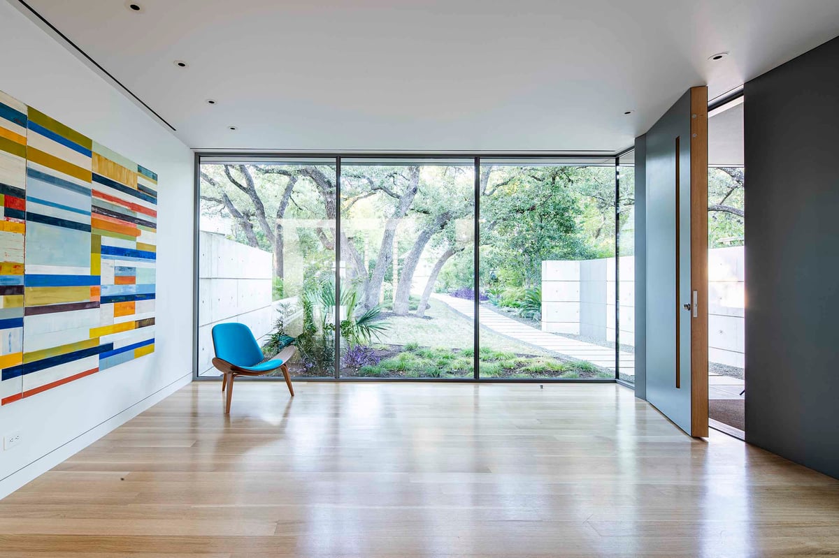 A gallery room with a colorful artwork and a glass wall to the garden