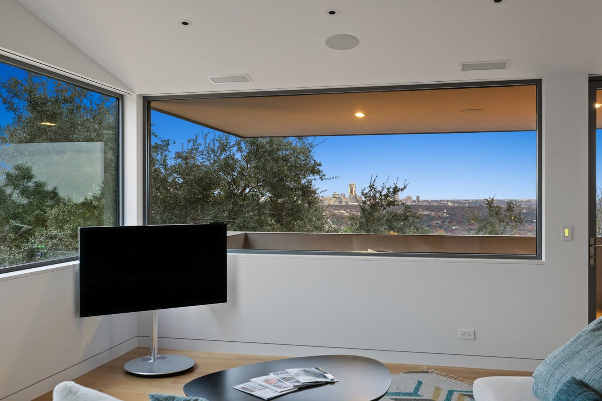 Upstairs lounge seen wide, a curved sofa facing a corner of windows over the treetops