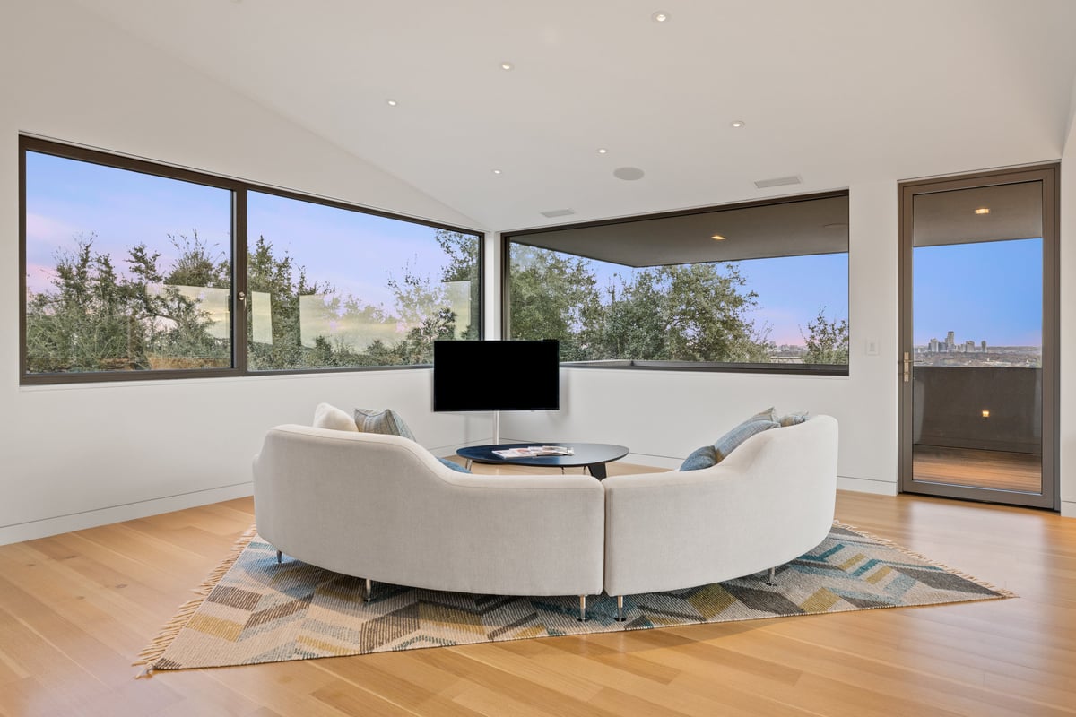 Upstairs lounge with a curved sofa under corner windows at dusk