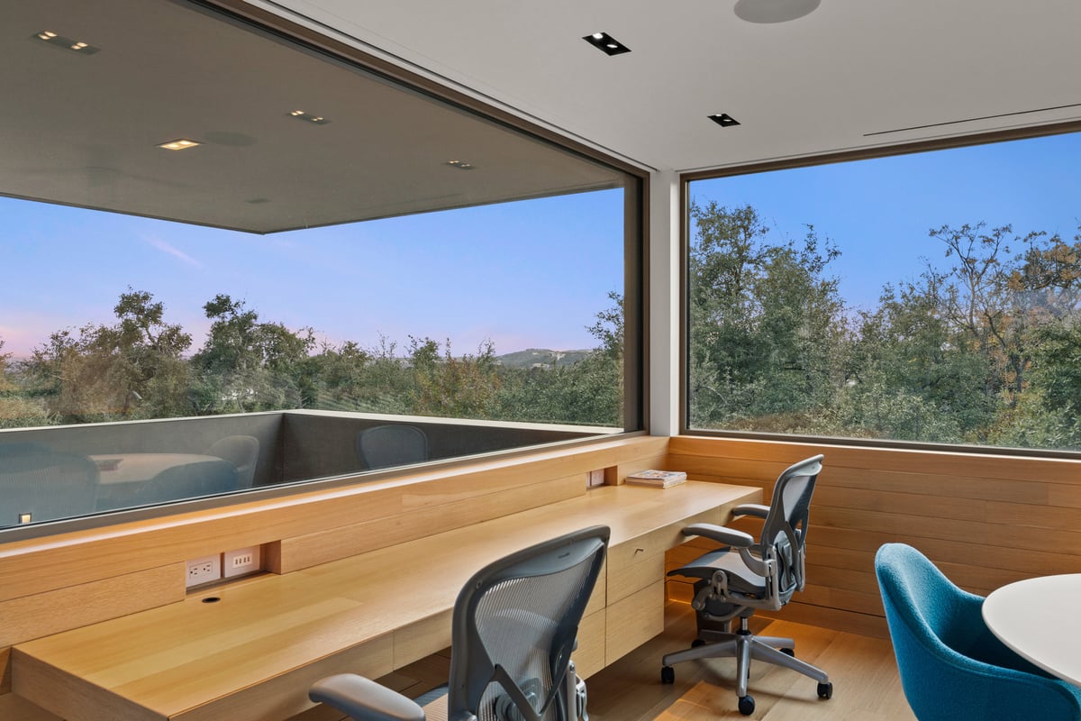 Built-in oak desks with task chairs under a wide corner window