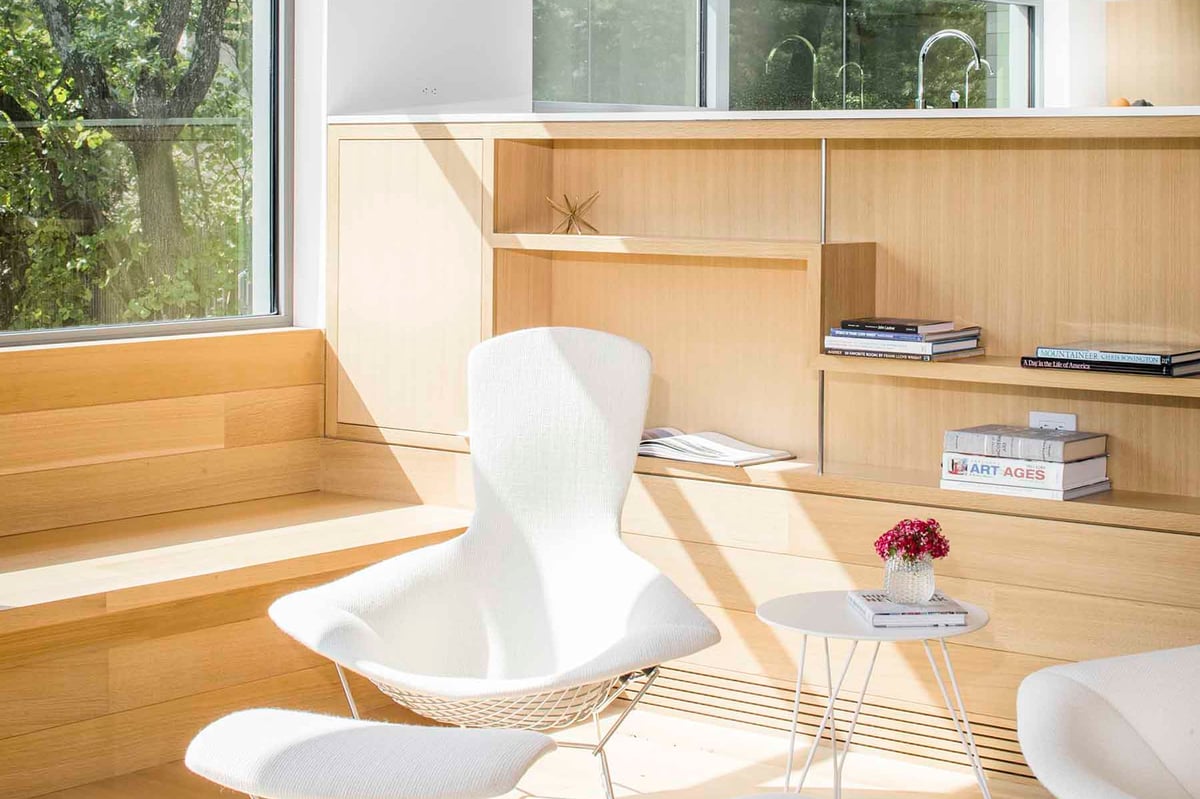 A reading nook with a white wire chair and oak built-ins by the window