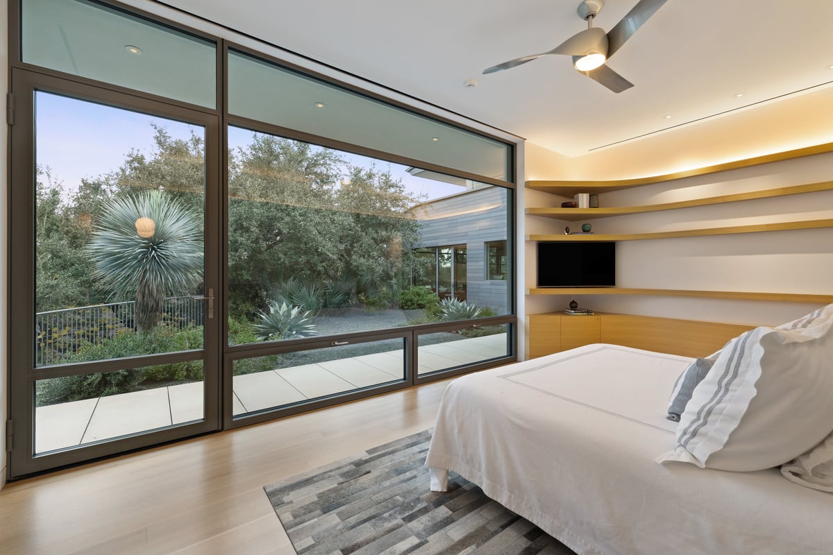 Primary bedroom with a wall of glass onto the treetops and a built-in media wall