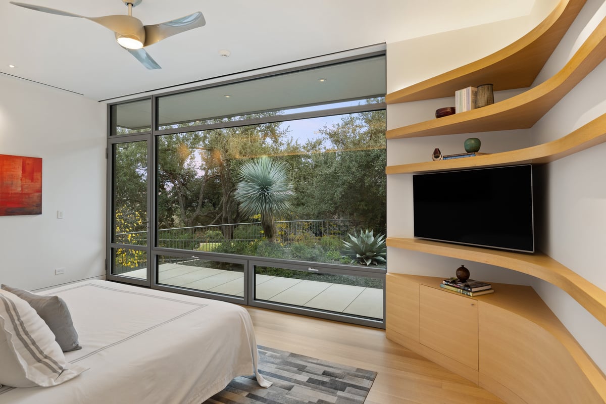 Primary bedroom corner with floating wood shelves and a garden view