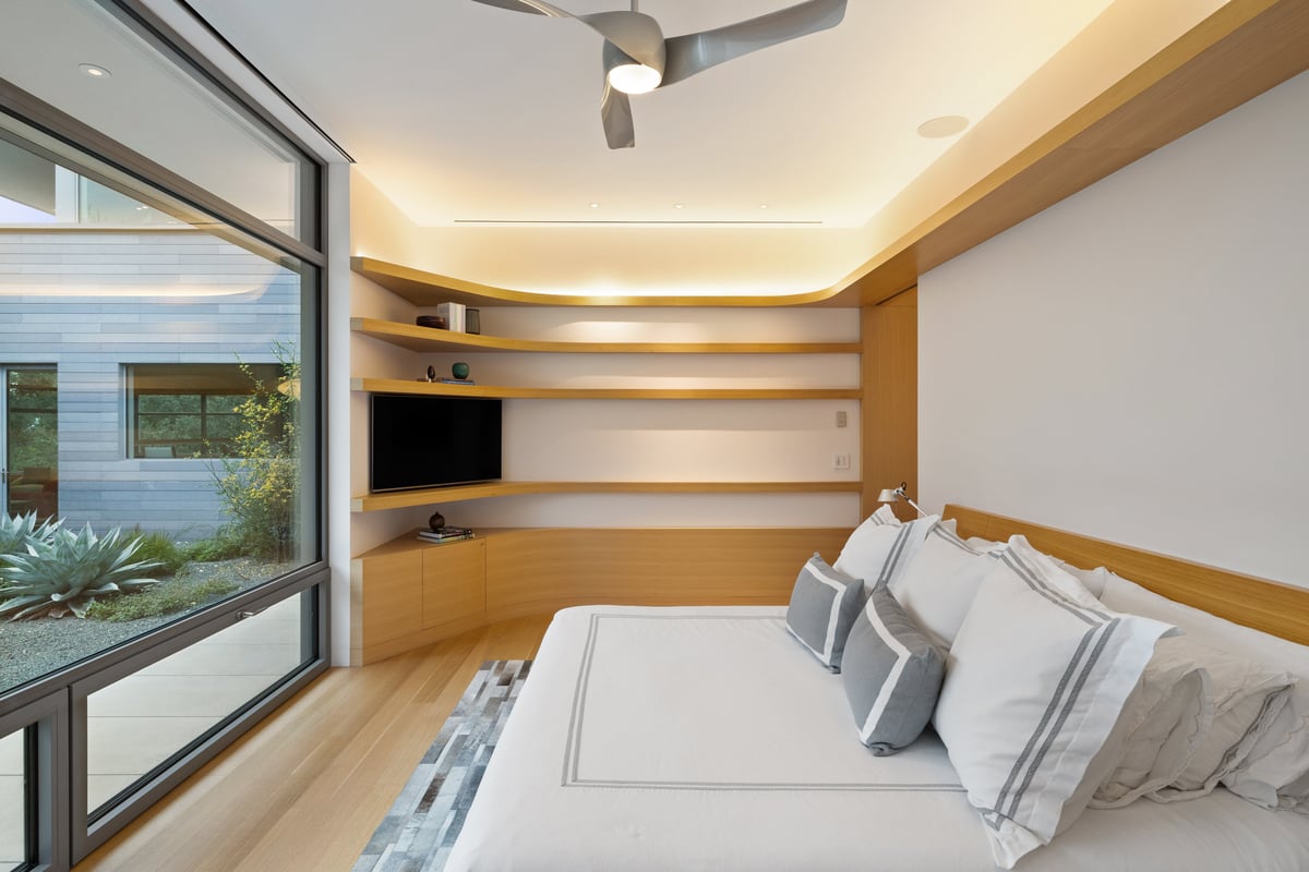 Primary bedroom with a corner window to a planted garden and wraparound shelves