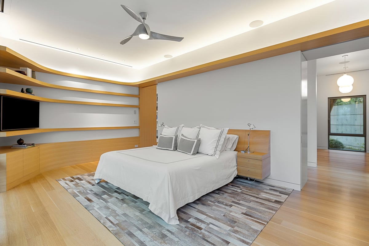 Primary bedroom seen wide, floating oak shelves and a door to the bath