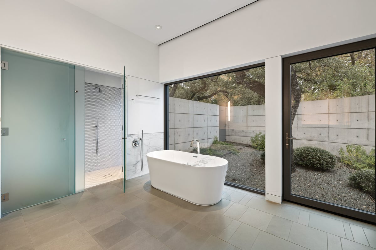 Primary bath with a freestanding tub, glass shower and a walled garden outside