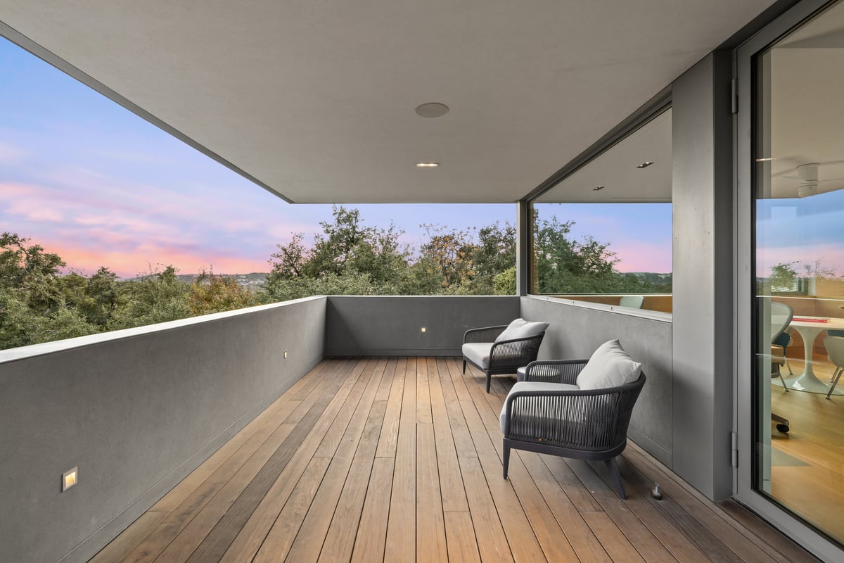 Covered terrace at dusk with lounge chairs and a view over the tree canopy