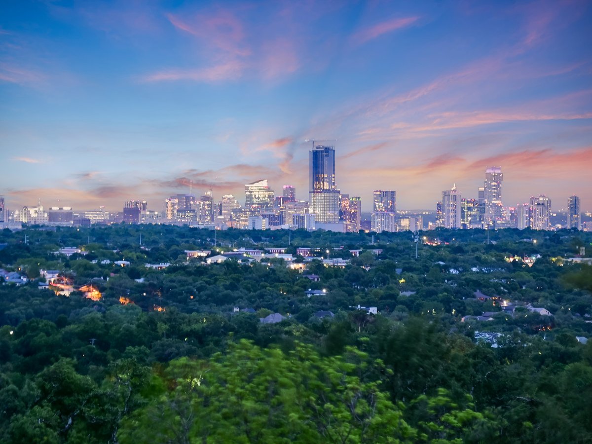 Downtown Austin skyline at dusk above the tree canopy, seen from the house