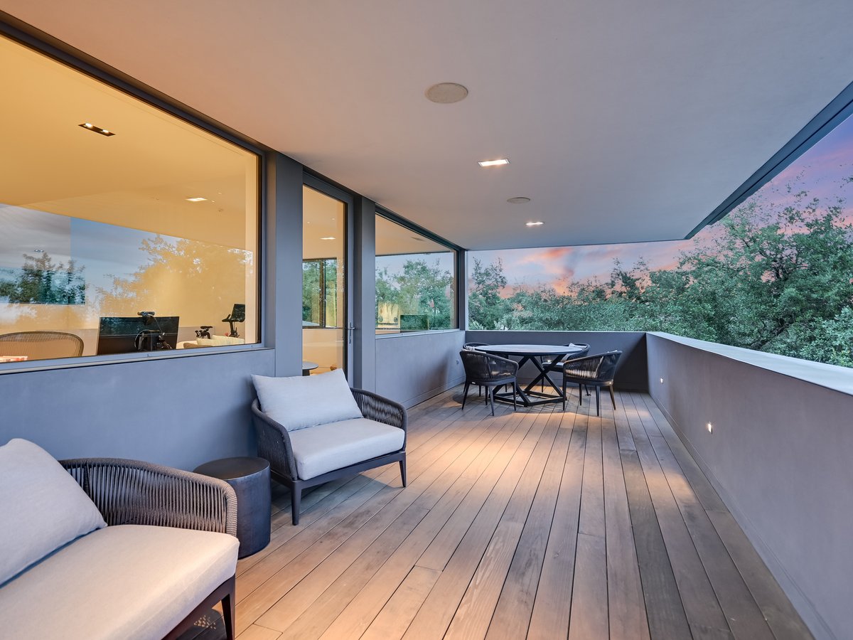 Covered terrace at dusk with lounge seating and a table beside the glass