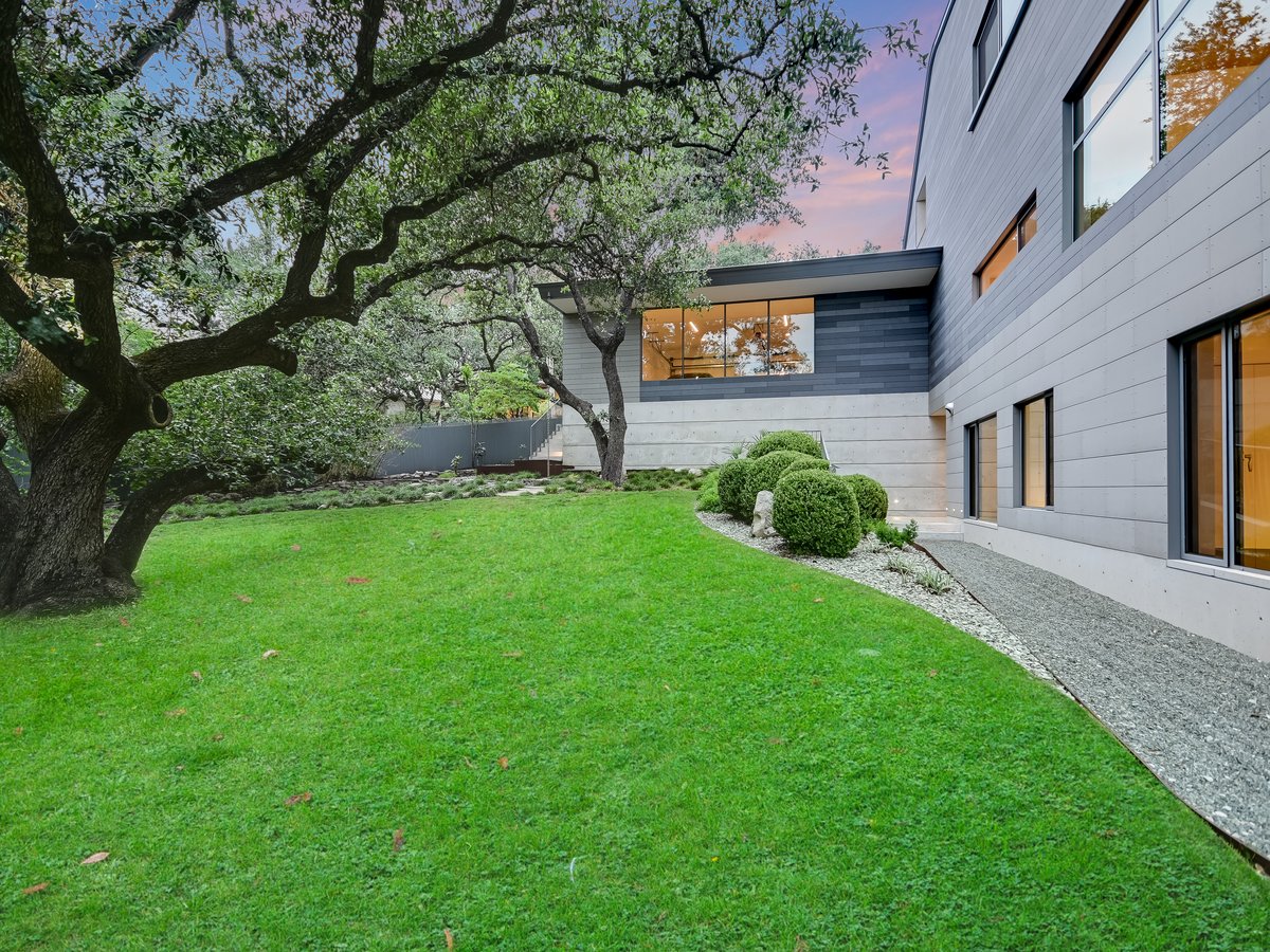 The rear lawn seen wide, oaks and the clad wings of the house
