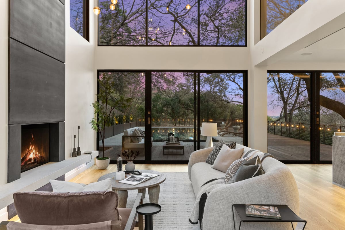 The two-story living room with a black fireplace wall and walls of glass at dusk