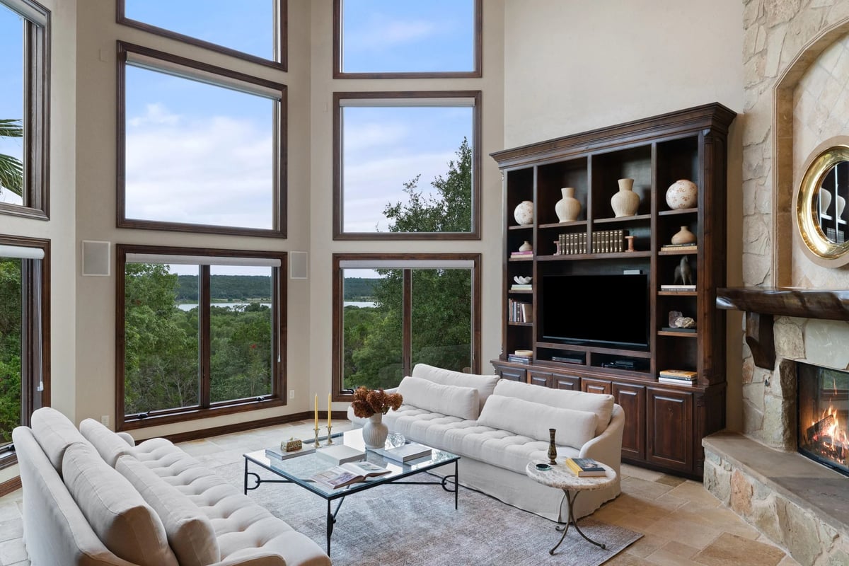 Living room with floor-to-ceiling windows framing Lake Georgetown views beside a stone fireplace