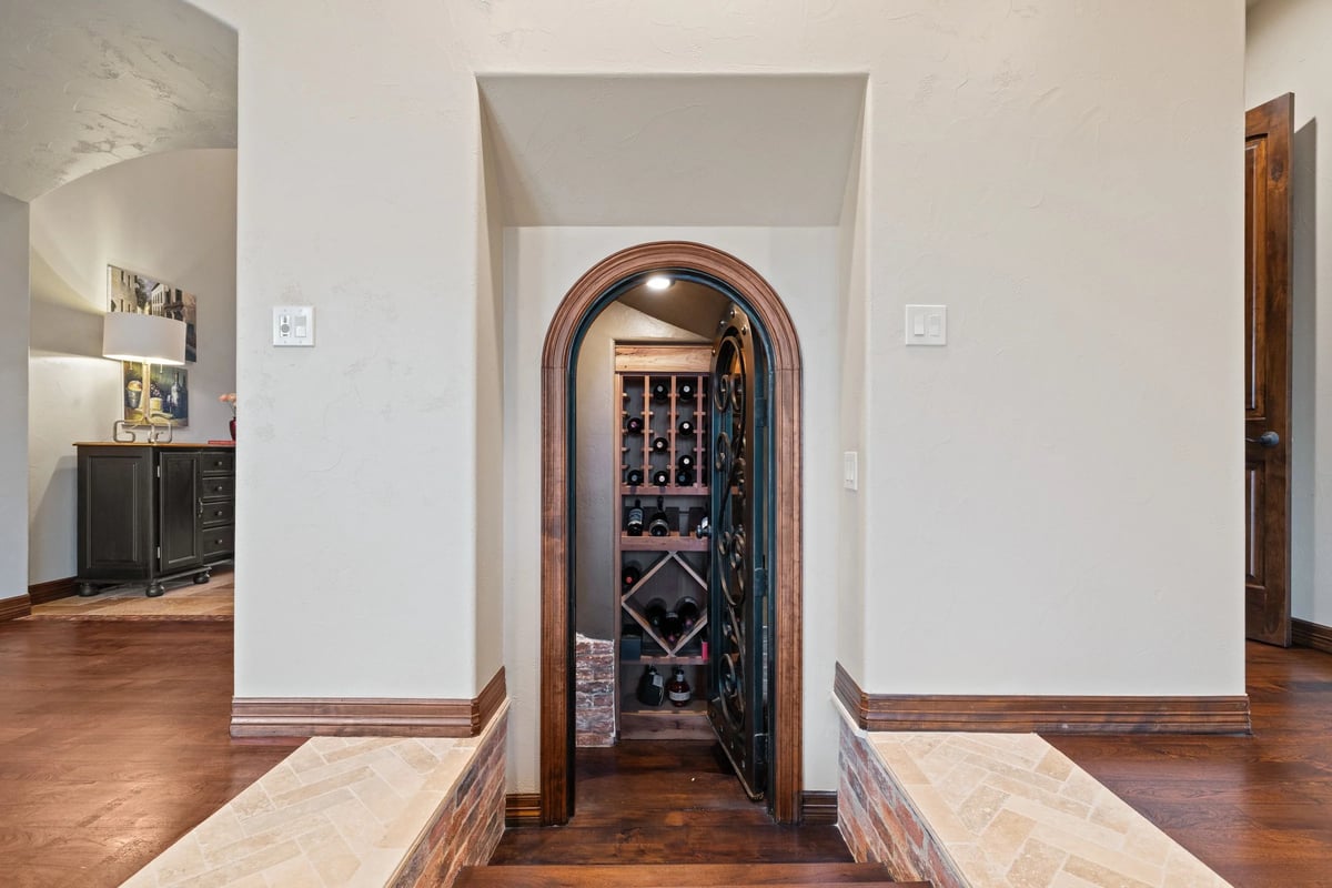 Arched wrought-iron wine cellar door opening to wood racks stocked with bottles