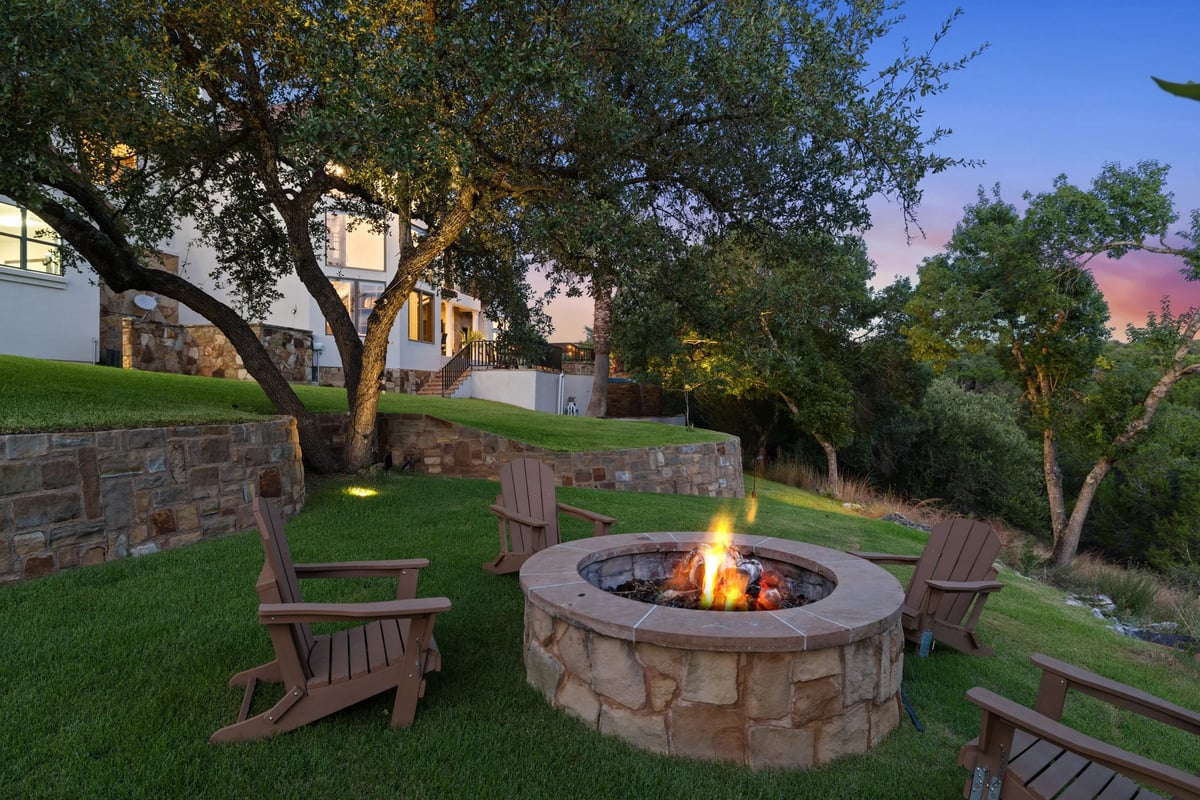 Stone fire pit with Adirondack chairs on the terraced lawn at dusk