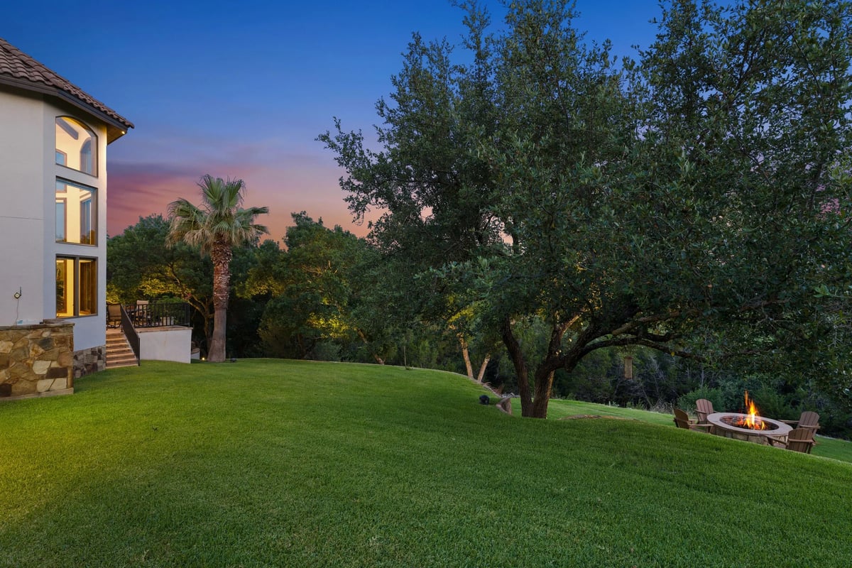 Backyard lawn beneath a mature oak tree with the fire pit in view at dusk