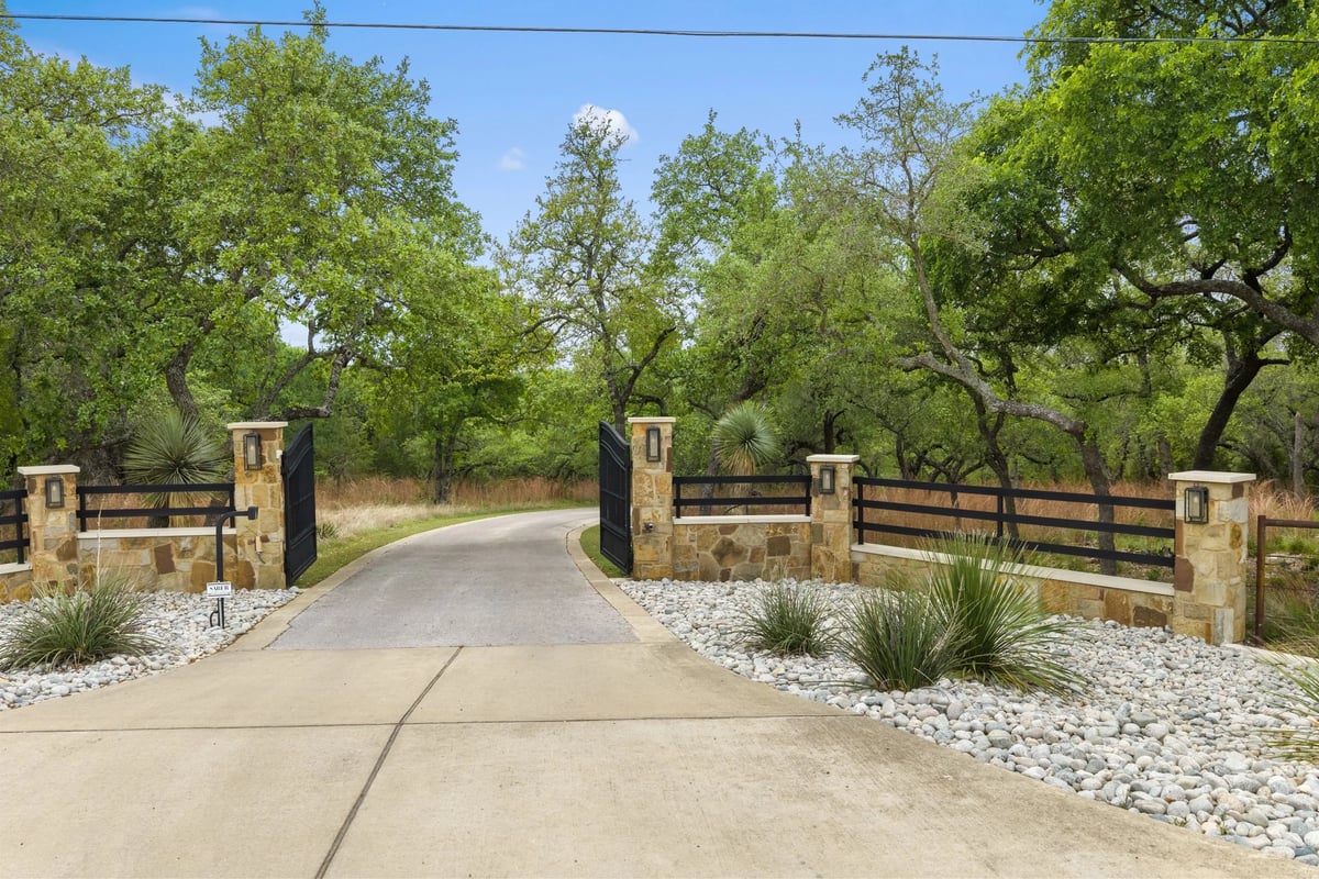 Gated stone entrance with wrought iron gates opening to the tree-lined drive